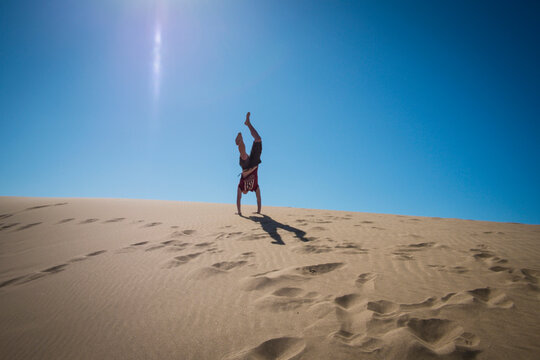 Caucasian teenage boy doing cartwheels on sand dune