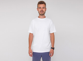 young stylish male doctor in white t-shirt and blue pants is standing straight and smiling on the white wall background. medical concept. free space , mockup
