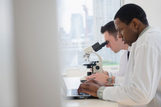 Scientists using laptop and microscope in lab
