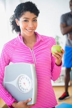 Woman holding apple and scale in gym