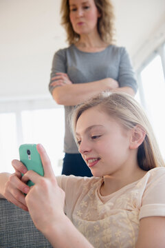 Caucasian mother watching daughter use cell phone