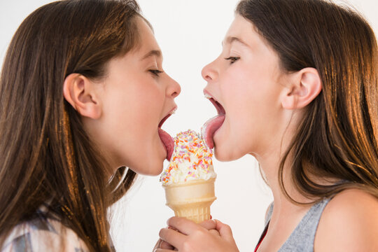 Caucasian twin sisters sharing ice cream cone
