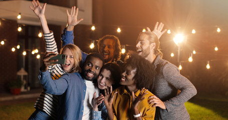 Mixed-races young happy and cheerful friends, men and women smiling and posing to smartphone while...