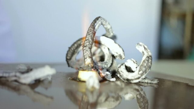 Chemical reaction of Pharaoh's serpent demonstration: conversion of Calcium gluconate to Hexamine fuel tablet. Black and white ash (the product of the burning reaction) rises from the flame. Close-up,