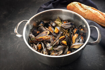 Freshly cooked mussels served in a steel pot with bread, on a dark slate table, delicious seasonal seafood meal, copy space, selected focus