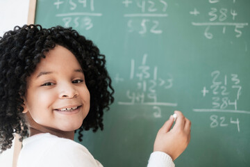 African American student writing on chalkboard in classroom