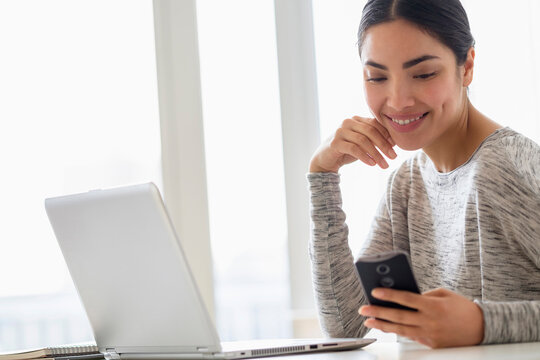 Hispanic woman using cell phone and laptop