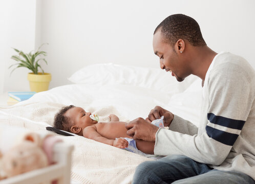 African man changing baby's diaper on bed