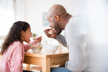 Father and daughter eating cereal at table