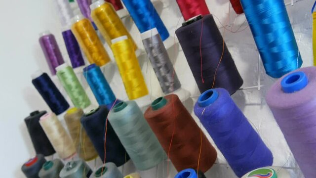 A row of multi-colored different threads for a sewing machine and overlock in a sewing workshop or atelier. Rows spools of thread of different colors in the industrial sewing machine