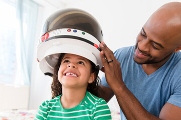 Father placing astronaut helmet on daughter