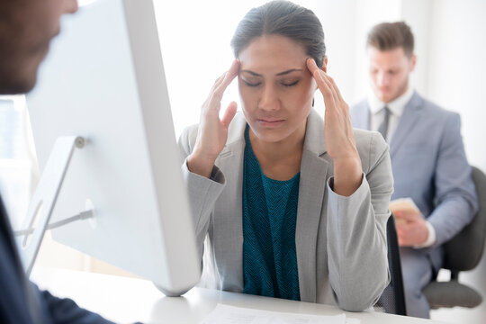 Businesswoman with headache rubbing temples in office