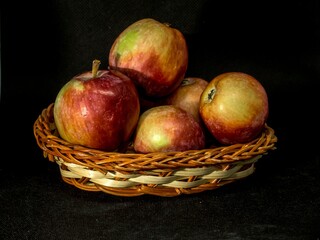 Red ripe apples in a wicker basket on a black background.