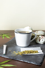 Fresh coffee, marijuana leaves, joints and chocolate donuts on wooden table with copy space top.