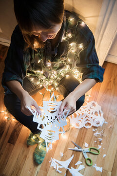 Mixed Race woman sitting on floor wrapped in string lights holding snowflake