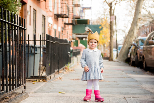 Smiling Caucasian baby girl wearing crown hat on city sidewalk
