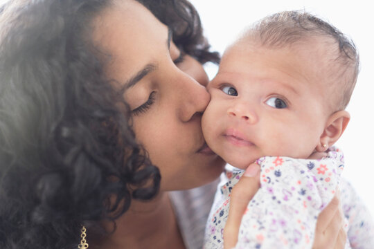 Hispanic mother kissing baby daughter on cheek