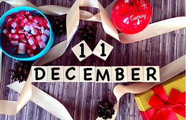 December 11 on wooden cubes.Next to it is a Christmas balloon, fir cones, a box on a wooden background.The first month of winter.Calendar for December.