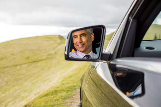 Reflection in mirror of smiling Caucasian businessman driving car