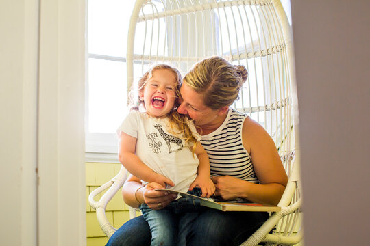 Playful Caucasian mother biting shoulder of daughter reading book