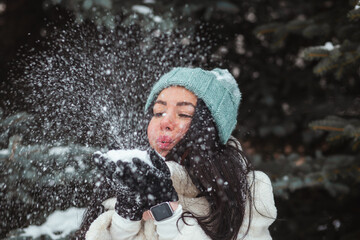 Winter fun, holidays and people concept - brunette woman in blue winter hat blowing snow from her gloves.