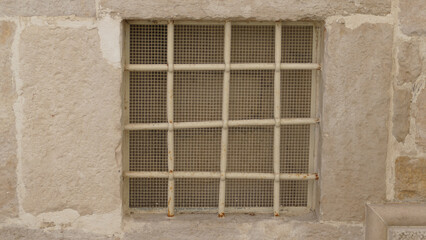 Vecchia finestra di um locale sotteraneo, chiusa con sbarre in ferro e rete metallica