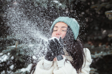 Winter fun, holidays and people concept - brunette woman in blue winter hat blowing snow from her gloves.