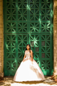 Smiling Hispanic girl wearing gown near green wall