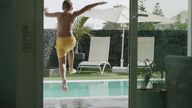 Slow motion shot of a child leaving the house and jumping into the swimming pool to refresh. So cool to have a swim at any time you want