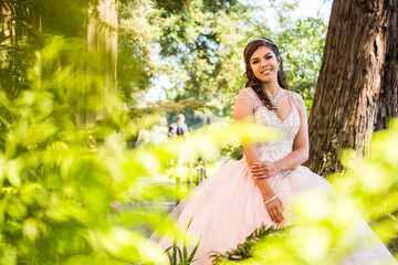 Portrait of a smiling Hispanic girl wearing gown near foliage
