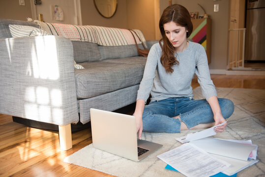 Caucasian woman sitting on floor paying bills with laptop