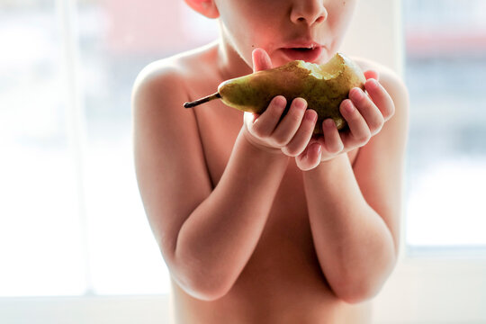 Naked Caucasian boy eating pear