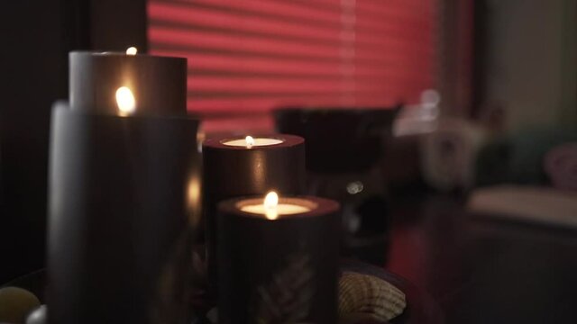 Close up of big dark burning candles creating romantic and calm atmosphere. Action. Details and decorations of room interior, chocolate aroma candles on the background of red blinds.