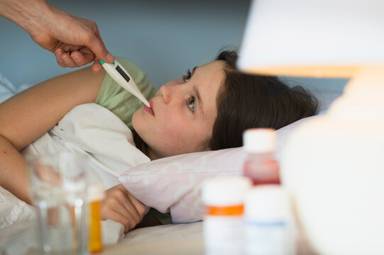 Sick girl (8-9) with thermometer in mouth