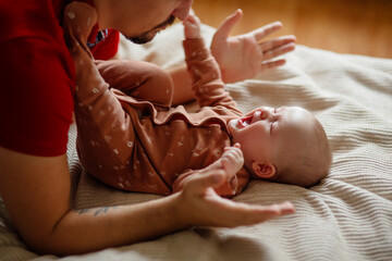 From above happy bearded man playing and talking with cute baby on comfortable bed at home