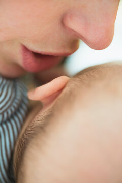 Close up of mother's mouth whispering into baby boy's(2-5 months) ear