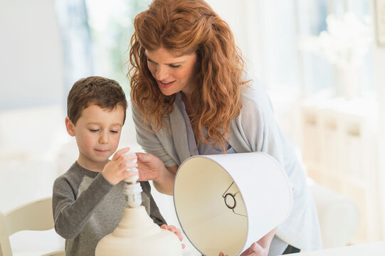 son (6-7) and mother changing lightbulb in table lamp
