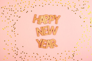 Beautiful wooden inscription happy new year on a paper background of champagne color surrounded by gold stars.