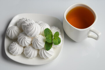 A few meringues on a plate with mint leaves and a mug of tea on the white table.