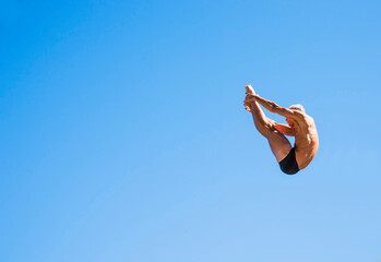 Athletic swimmer mid-air against blue sky
