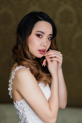 Obraz premium Gorgeous young asian woman in elegant dress looking at camera and window, morning of bride, wedding