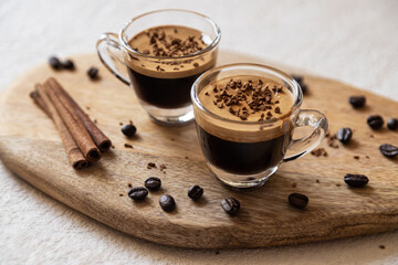 Two cups of coffee espresso. coffee beans, cinnamon sticks on a wooden board, light background