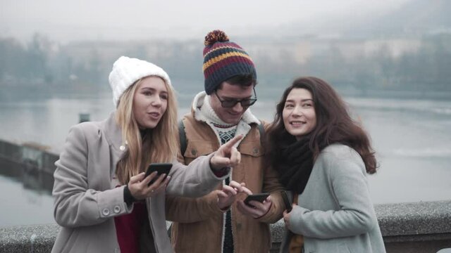 Group of teenage friends finding out directions on the streets with phone. Teenagers walking around european town during christmas holiday season. Beautiful city on winter and river on background.