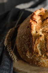 The handcrafted tartin bread lies on a wooden surface next to wheat ears. Farming and home baking concept