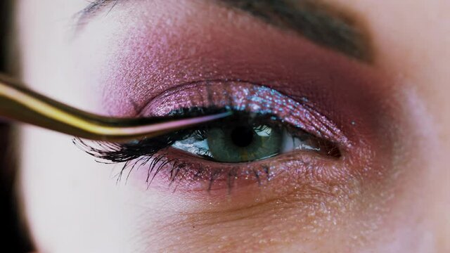 Woman removes false eyelashes with tweezers. Amazing green eye macro view make-up with shining shadows. Beauty, art, glamour concept.