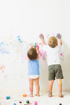 Children (2-3) painting on wall, rear view