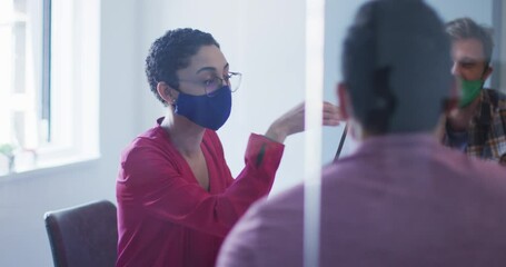 Diverse colleagues wearing face masks discussing together in meeting room at modern office - Powered by Adobe