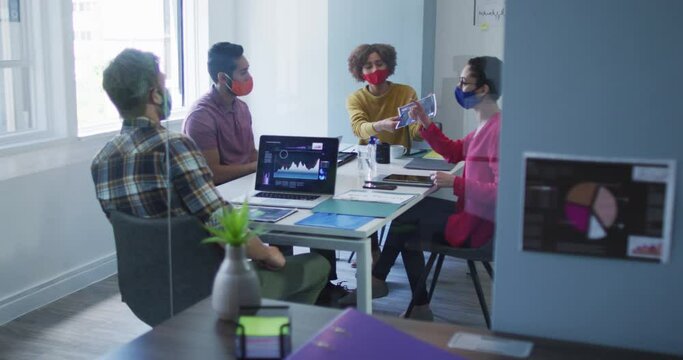 Diverse colleagues wearing face masks working together in meeting room at modern office