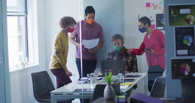 Diverse colleagues wearing face masks working together in meeting room at modern office