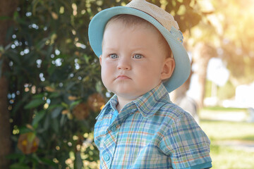 portrait of a beautiful blue-eyed little boy, in a hat, against the background of green foliage. Rrebenok with a serious, thoughtful look looks in the distance. Horizontal photo,